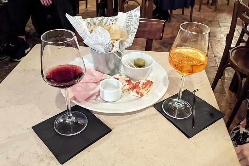Aperitivo-Gedeck mit verschiedenen Snacks, dazu ein Glas Rotwein und ein Aperol Spritz