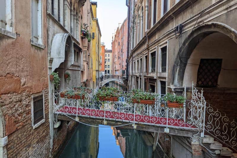 Mit Blumen dekorierte, schmiedeeiserne Brücke in Venedig mit mehreren Stufen