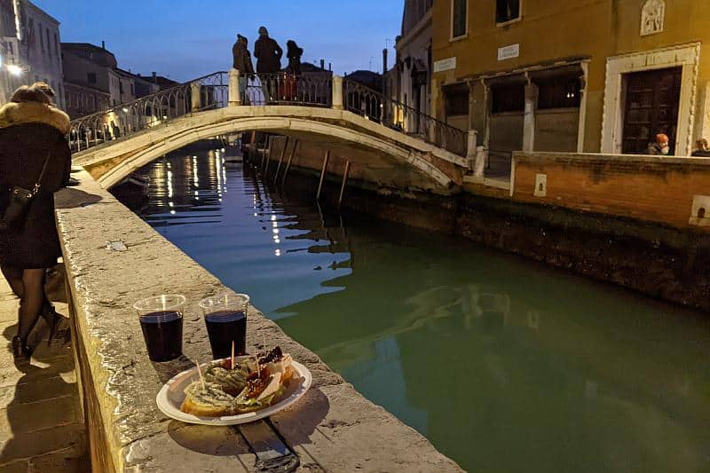Zwei Becher mit Wein und belegte Brote auf einer Mauer an einem Kanal beim Aperitivo in San Trovaso in Venedig