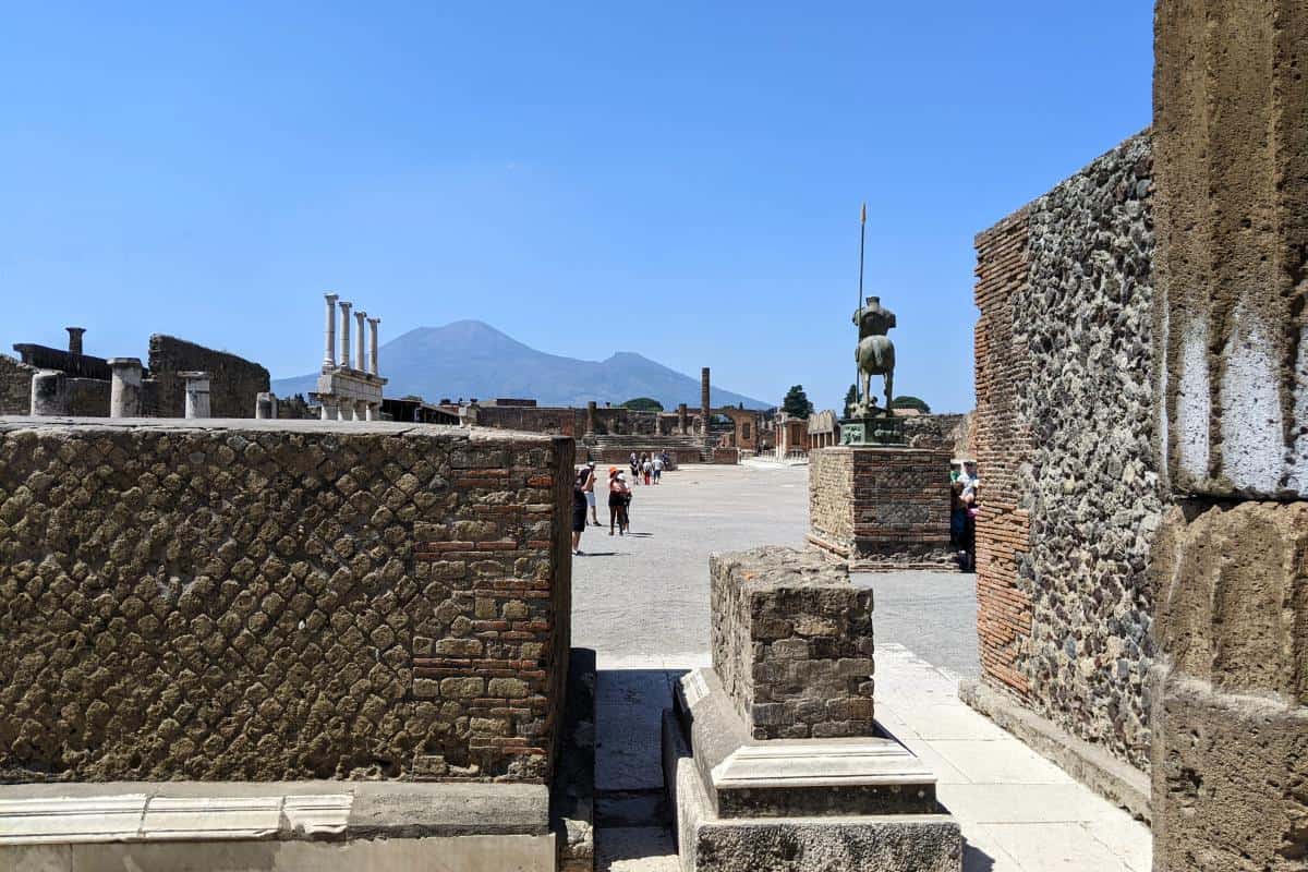 Hauptplatz von Pompei mit Skulpturen, Säulen und dem Vesuv im Hintergrund