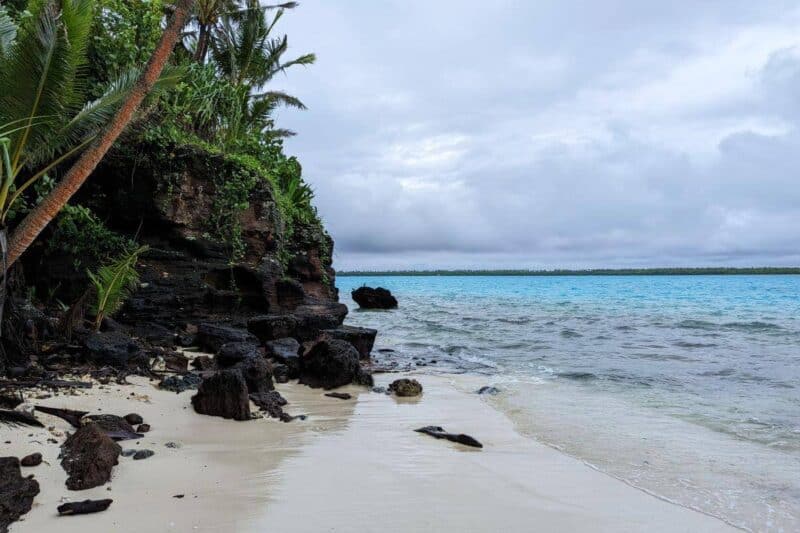 Schwarze Felsen vor blauem Wasser am Strand von Moturakau