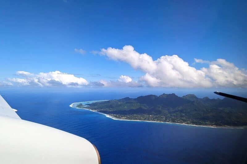 Blick aus dem Flugzeug auf die bergige,  grün bewaldete Insel Rarotonga im blauen Südpazifik
