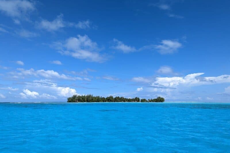 Die leuchtend blaue Lagune von Bora Bora mit einem kleinen, bewaldeten Motu im Hintergrund