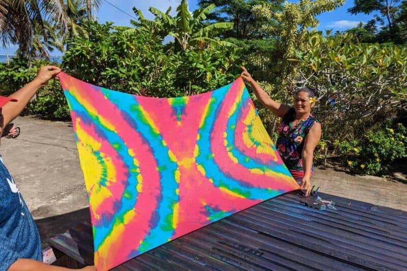 Eine Polynesierin hält einen frisch bunt gefärbten Pareo in die Sonne