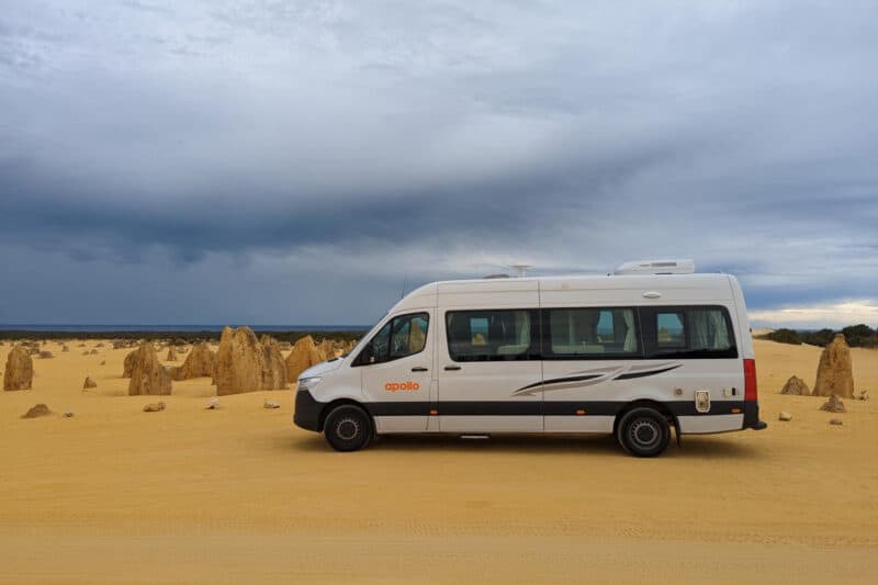 Campervan in einer Wüstenlandschaft mit den Felsnadeln der Pinnacles im Hintergrund