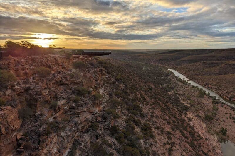 Eine Metallplattform ragt über die breite Schlucht des Murchison River mit tiefstehender Sonne im Hintergrund 