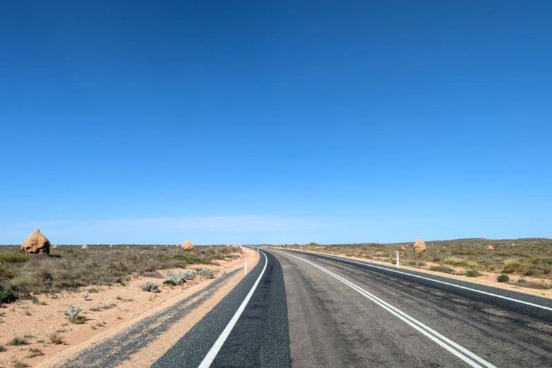 Von Termitenhügeln gerahmte Landstraße in Westaustralien