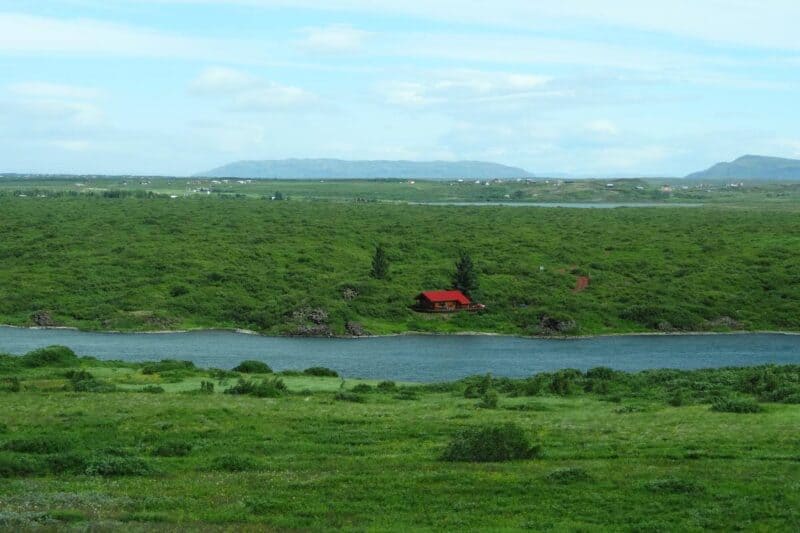 Rot gedecktes Ferienhaus an einem Fluss inmitten grüner Landschaften