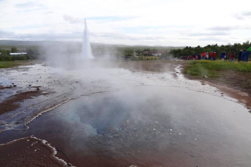 Die Wassersäule des Strokkur schießt hinter einem dampfenden Wasserbecken empor