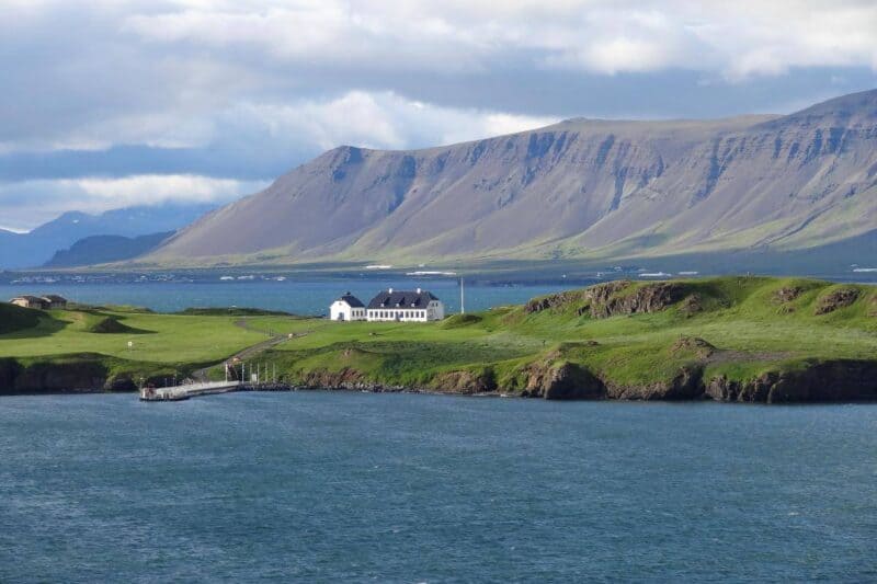 Ein weißes Häuschen steht auf einer grünen Insel im Meer vor Reykjavik