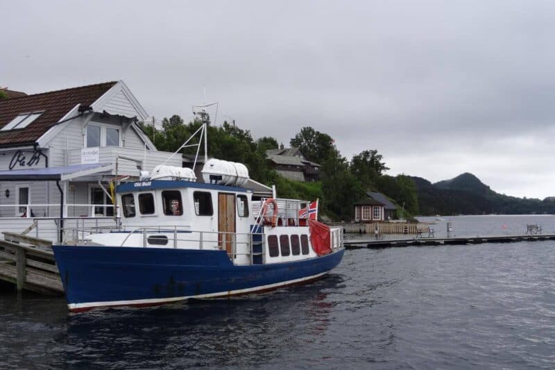 Fischerboot im Fjord vor einem weißen Holzhaus