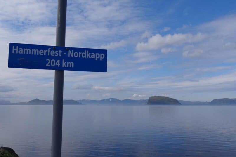 Felsen im Meer vor Hammerfest und ein Schild mit der Aufschrift "Hammerfest - Nordkapp 204 km"
