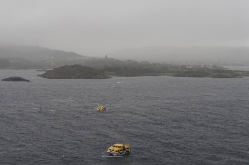 Wolken- und regenverhangener Blick auf die Lofoten mit kleinen gelben Tenderbooten auf dem aufwühlten Meer