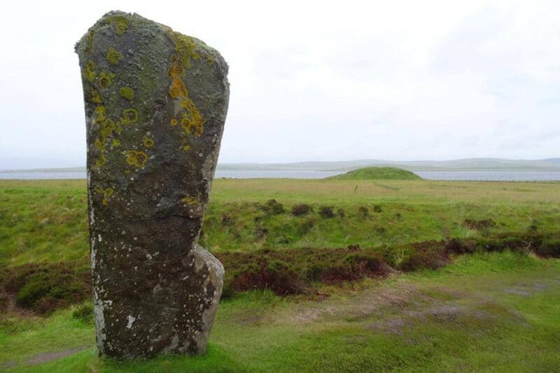 Steinsäule im Ring of Brodgar mit Hügelgrab im Hintergrund