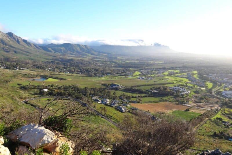 Blick ins Tal vom Ou Kaapse Weg mit Häusern, Feldern und den Steenberg Mountains im Hintergrund