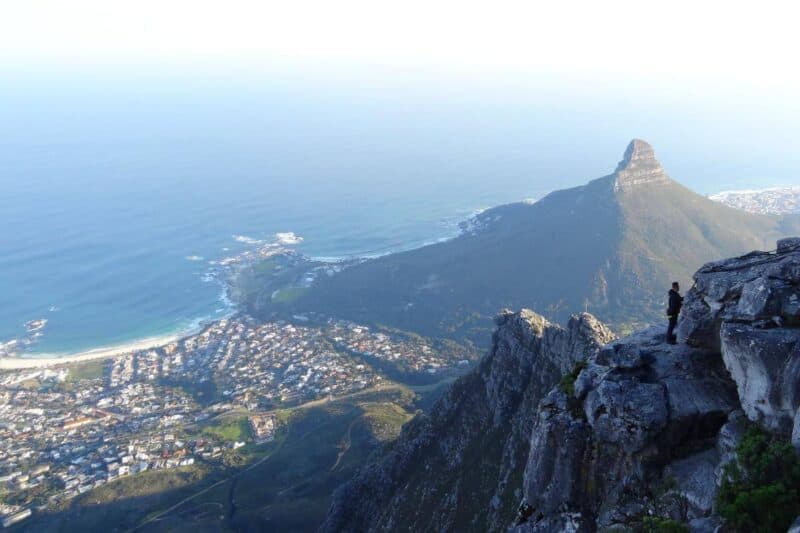 Blick vom Tafelberg auf einen Strandvorort, das Meer und einen Kletterer in den Felsen