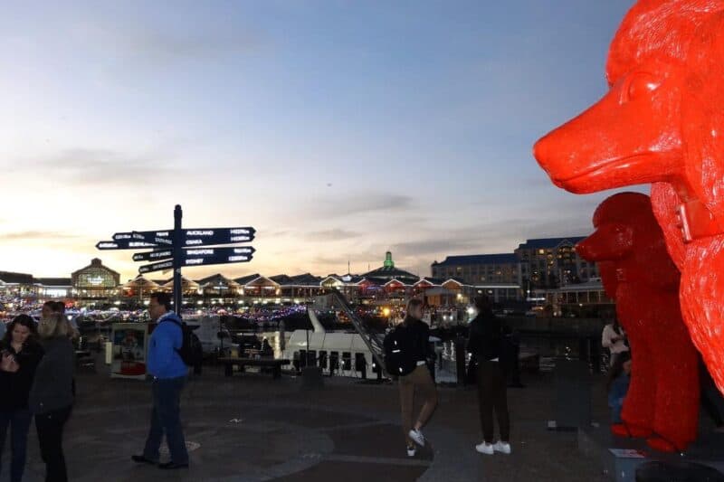 Nächtliche Victoria & Alfred Waterfront mit beleuchteten Gebäuden und einem Wegweiser