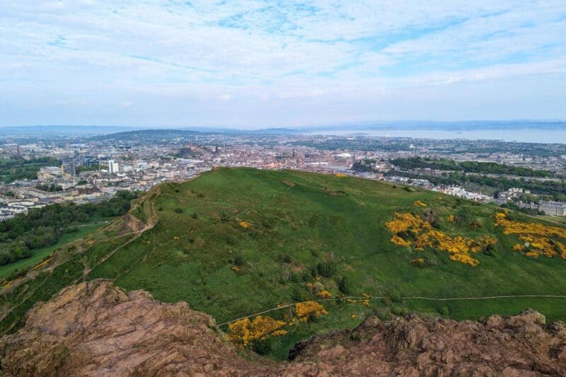 Blick über den "Vorhügel" Salisbury Crags und die Innenstadt von Edinburgh vom Gipfel des Arthur's Seat