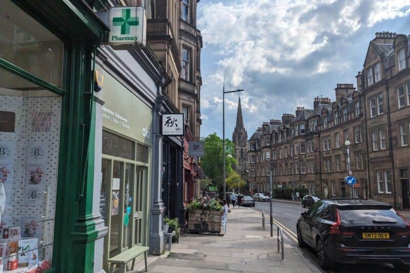 Hölzerne und steinerne Fassaden der Geschäfte und Restaurants in Bruntsfield mit Kirchturm im Hintergrund