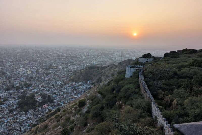 Aussicht über das Häusermeer von Jaipur mit Stadtmauer und Sonnenuntergang