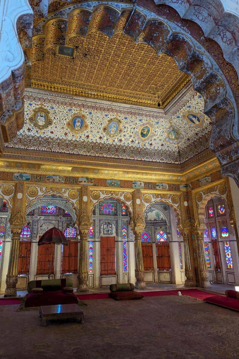 Blick durch einen Marmorbogen auf eine mit Gold verzierte Decke in einem Prunkraum im Merangarh Fort